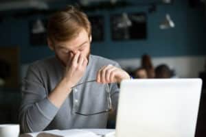 Man working on computer, rubbing his eyes from eye fatigue after staring at screen