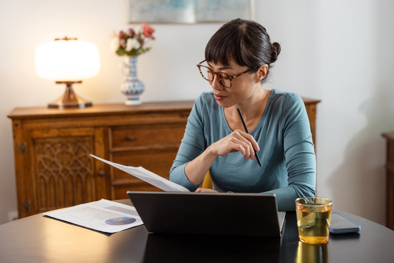 Woman pulling at her eyelid skin Woman wearing reading glasses reviewing paperwork at a laptop, illustrating age-related near vision changes that may lead adults to consider refractive lens exchange.